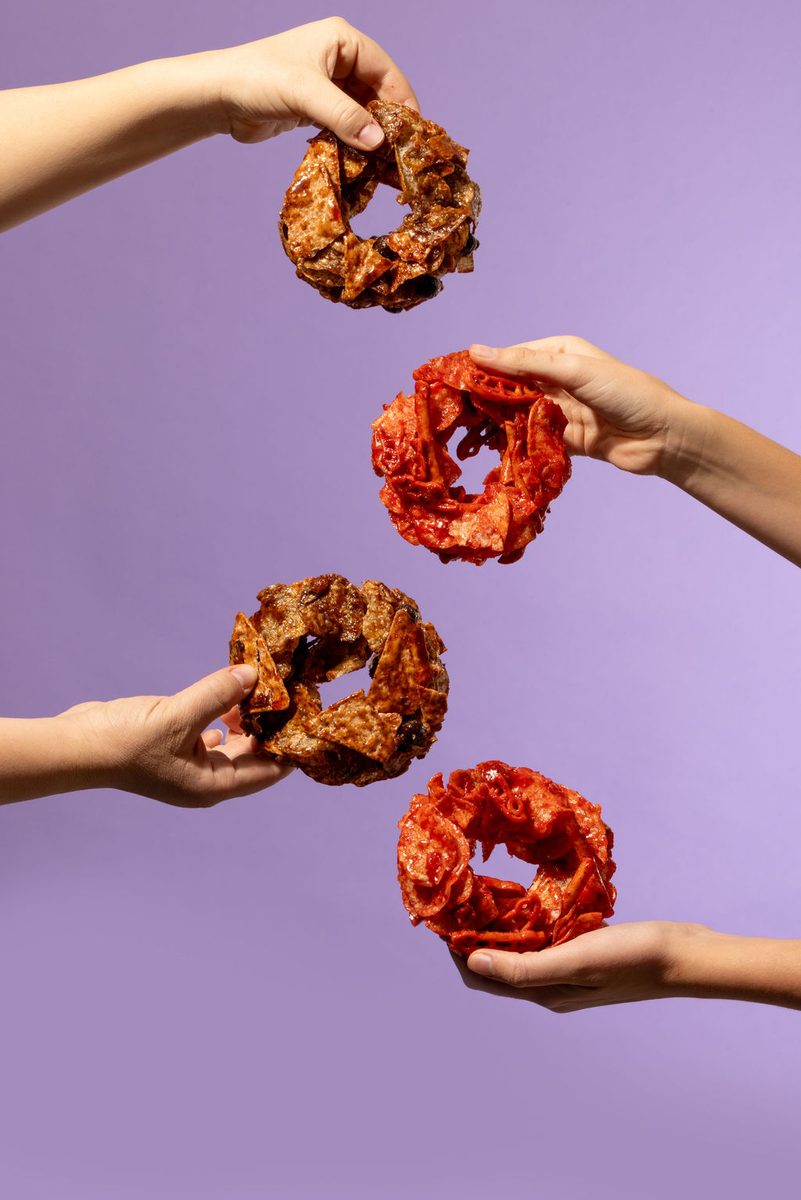 Cuatro manos con roscas Flaming Hot y Salsas Negras, fondo morado