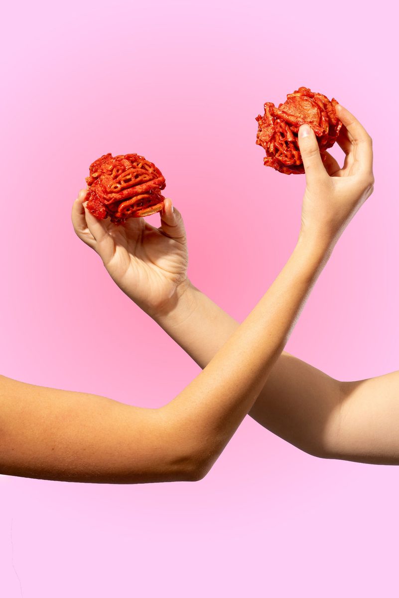 Dos bites Flaming Hot sostenidos sobre fondo rosa